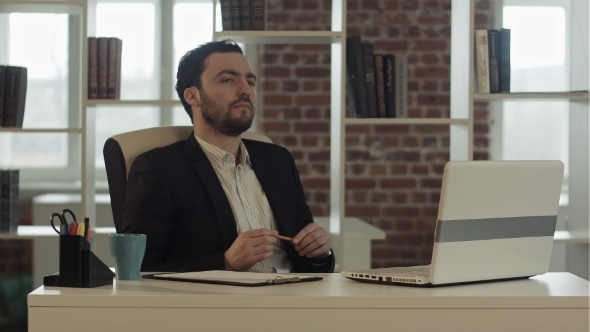 Young Business Man Sitting At Office Looking Up alt