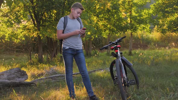 Boy in Park After Riding Bicycle Uses Phone at Sunset, Watching Social Networks or Chatting. Concept