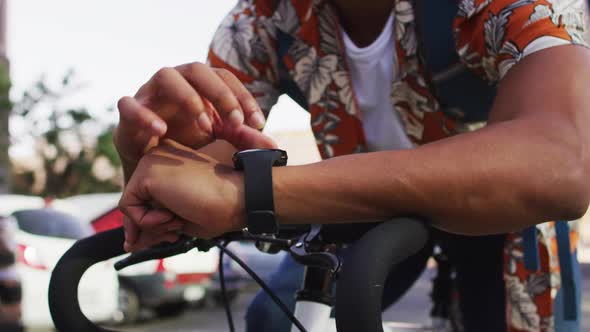 African american man in city, sitting on bike in street using smartwatch