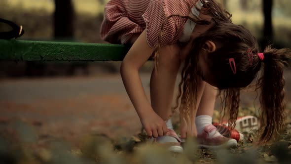 Kid  Sitting And Tying Sneakers Shoes. Children Sitting In Park And Preparing To Walk With Parents.