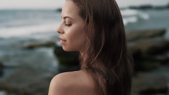 Side View Portrait of Woman Looks at Ocean Gently Runs Hand Over Her Shoulder