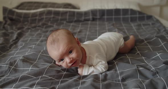 Little Newborn Baby Boy Lies on a Bed on His Front Trying to Hold His Head Up