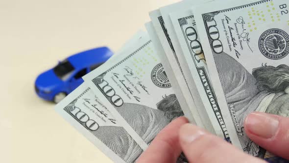 Hands Close-up Counting Money on the Background of a Small Car Model. The Concept of Buying Cars