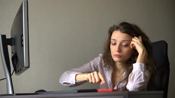 Tired Young Woman with Curly Hair and White Shirt is Working at the Office and Using Her Red