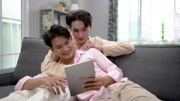 Cute Male Gay Couple Spend Time at Home. Happy lgbtq couple Lying Down on a Sofa and Use a tablet