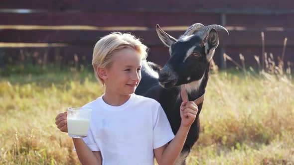 A Boy Drinks Goat Milk From a Mug Next To His Goat