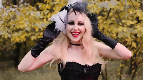 A beautiful girl in the image of a witch in black gloves with black eyes and red lips. Smiles playfu