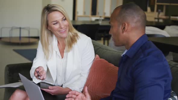 Two diverse business colleagues using laptop laughing and discussing in a casual meeting