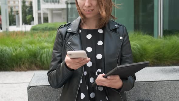 Modern Business Woman Uses a Mobile Phone and Holding a Tablet in Her Hands Waiting for a Client on