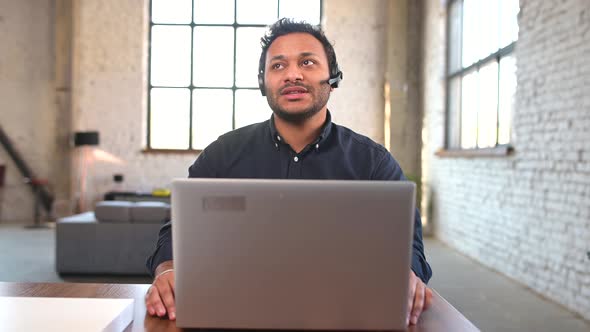 Concentrated Hindu Man Wearing Wireless Headset Using Laptop for Remote Connection