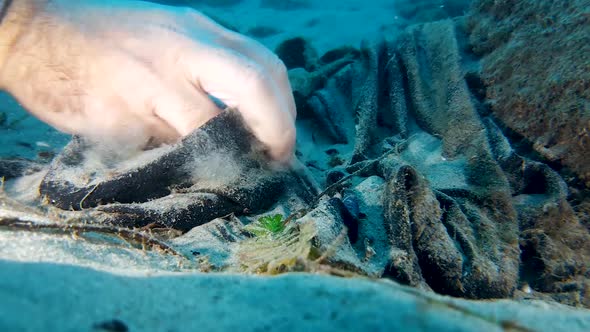 Picking up ocean trash underwater causing the sand to be stirred up near the camera