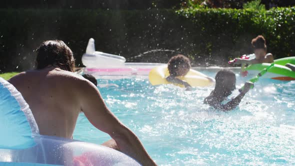 Diverse group of friends having fun playing with water guns on inflatables in swimming pool