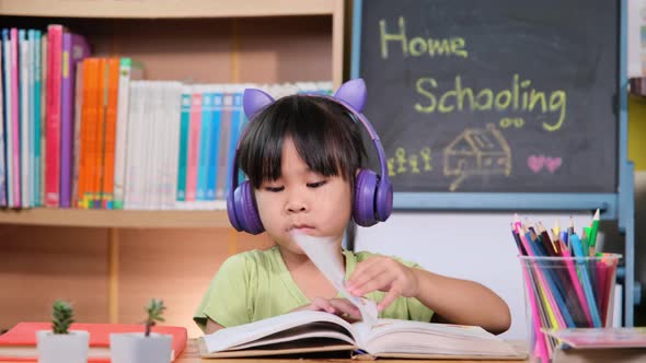 Cute little girl with headphones listening to audio books with english learning books on the table. alt