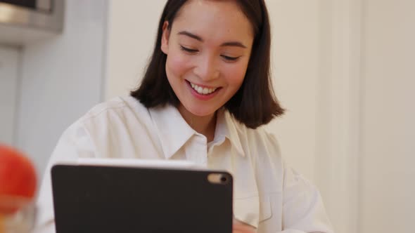 Smiling Asian woman writing something and talking by video call on the tablet