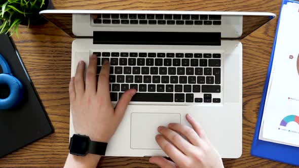 Hands Typing on a Laptop on a Desk Next To Business Reports and Diagrams