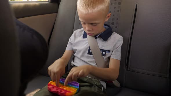 Little Boy Holds an Antistress Toy Pop It in His Hands While Sitting in the Car