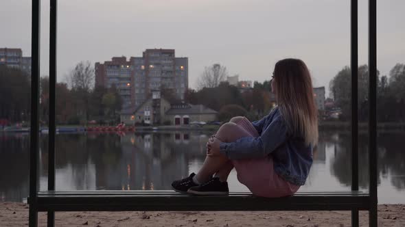 A Lonely Young Girl Sits on a Bench in the City on an Autumn Evening