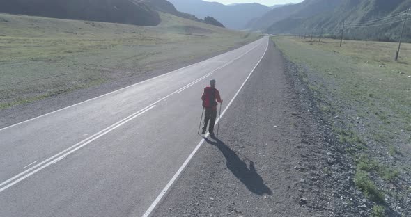 Flight Over Hitchhiker Tourist Walking on Asphalt Road. Huge Rural Valley at Summer Day. Backpack