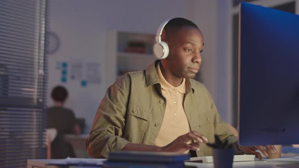 Black Man in Headphones Working on Computer in Office at Night