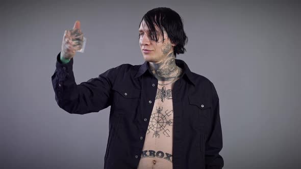 Young Tattooed Caucasian Man Holding Transparent Pack with White Pills Posing at Grey Background