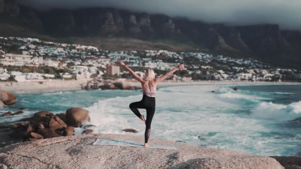 Beautiful and healthy female doing a yoga pose in front of a amazing blue seascape with misty mounta