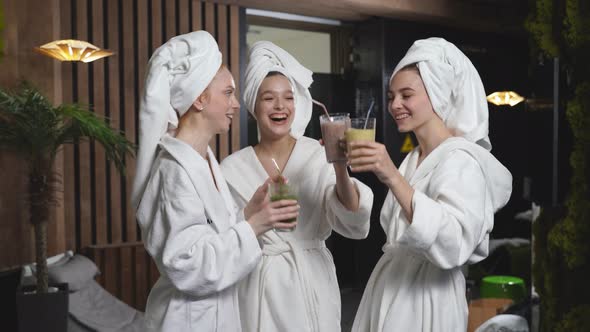 Caucasian Women Relaxing and Drinking Juicy Beverage Smoothies in Robes During Wellness Weekend