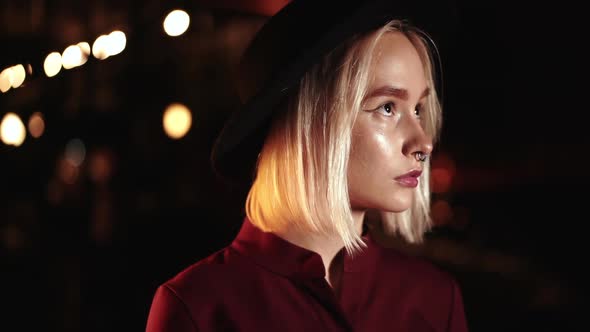 Portrait of Trendy Hipster Woman with Blond Hairstyle Standing on City Street at Night. Hat, Nose
