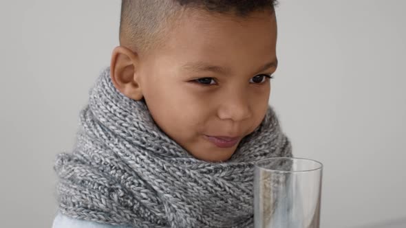 Little Black Boy Wearing Neck Snood Scarf Drinking Clean Water From Glass