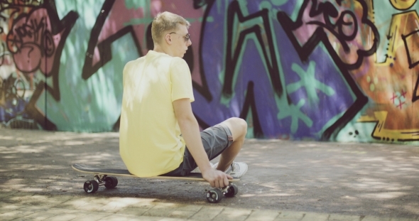 Man Sitting On Longboard And Looking Into Distance