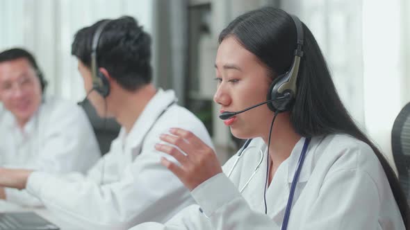 Woman Doctor Working As Call Centre Agent Speaking To Customer While Colleagues Are Talking