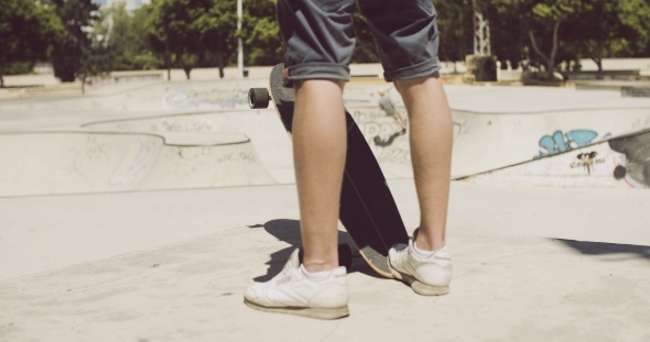 Man Standing At a Skate Park With His Longboard