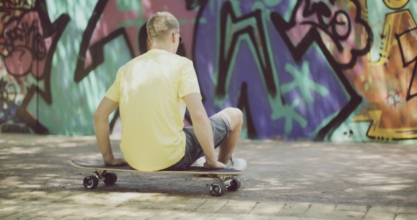 Man Sitting On Longboard And Looking Into Distance