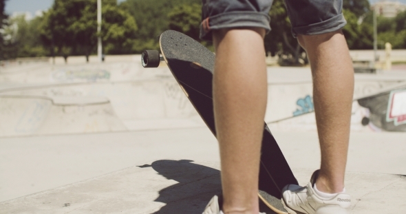 Man Standing At a Skate Park With His Longboard