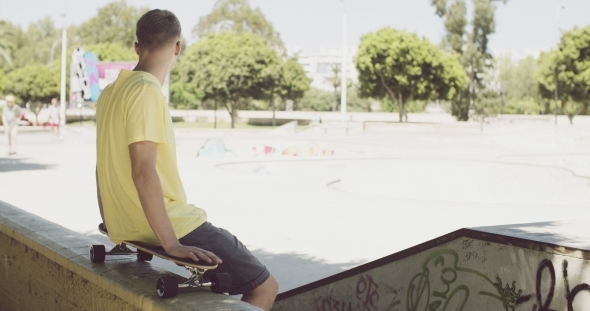 Man Sitting On a Skateboard Balanced On a Wall