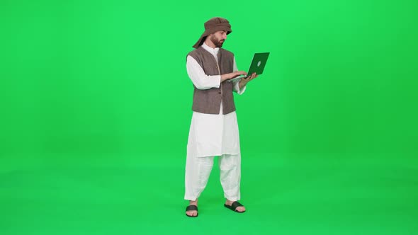 A Man of Arab Appearance in Traditional Clothes Uses a Laptop to Surf the Internet While Stands