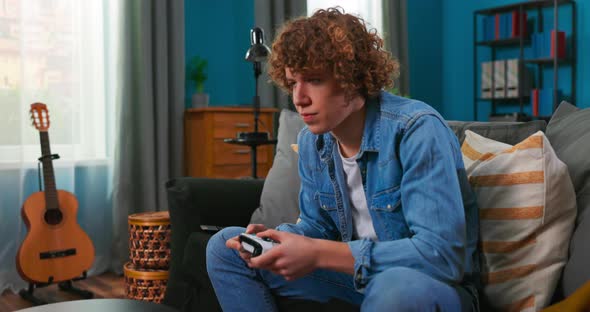 Portrait of Young Handsome Gamer Boy Sitting on Sofa and Playing in Video Games on