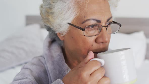 Close up of african american senior woman drinking coffee while sitting on the bed at home