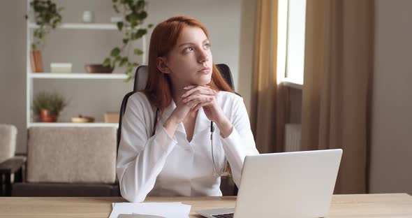 Focused Young Female Practitioner Doctor or Nurse in White Coat with Stethoscope Sitting at