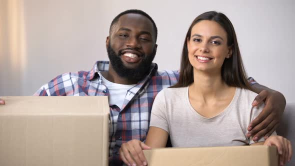 Happy Mixed-Race Couple Holding Carton Boxes, Ready to Move in New Apartment