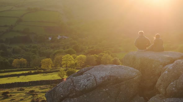 Couple watching the sunset sitting on rock formations in Dartmoor national park moorland, England, o