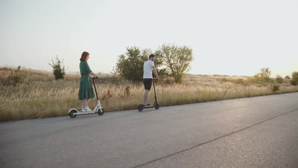 Couple Riding in Column on Electric Scooters Man Turning and Looking After Girl