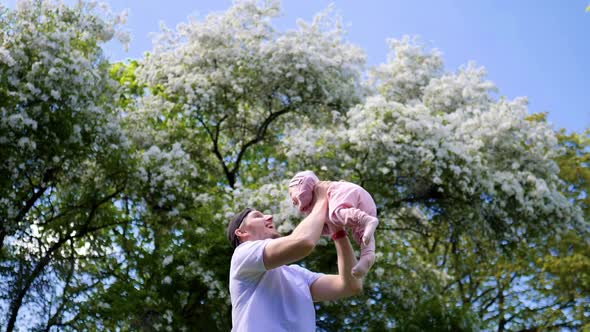 Young Man Throwing Baby High In Air Outdoors In Park