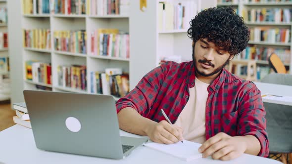 Focused Clever Arabian or Indian College Student Sits at Table with Laptop in University Library