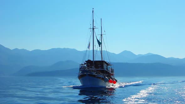 Medium shot of a sailboat heading towards camera with blue mountains silhouetted on the horizon