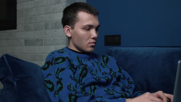 Relaxed Man Yawning Student Freelancer Using Laptop Device Leaning on Sofa at Home Office, Focused