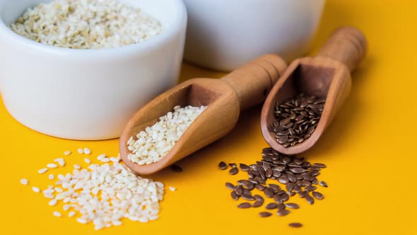 Zoom in Out Wooden Spoons with Flax and Sesame Seeds Lies in a White Mortar on a Yellow Background