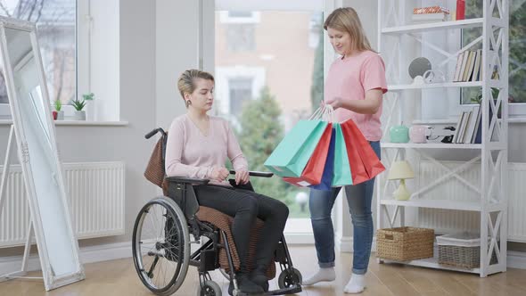 Wide Shot Portrait of Smiling Young Woman Bringing Shopping Bags for Paraplegic Friend