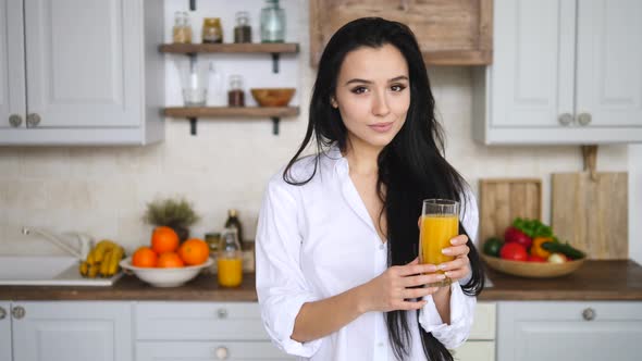 Young Cheerful Girl Holding A Glass Of Orange Juice On Kitchen.