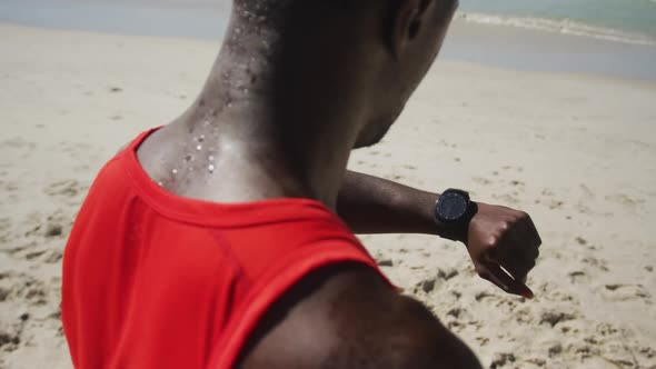 African american man checking his smartwatch, taking break in exercise outdoors by the sea