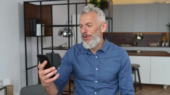 Grey Haired Businessman in Smart Casual Wear is Using Smartphone for Video Connection